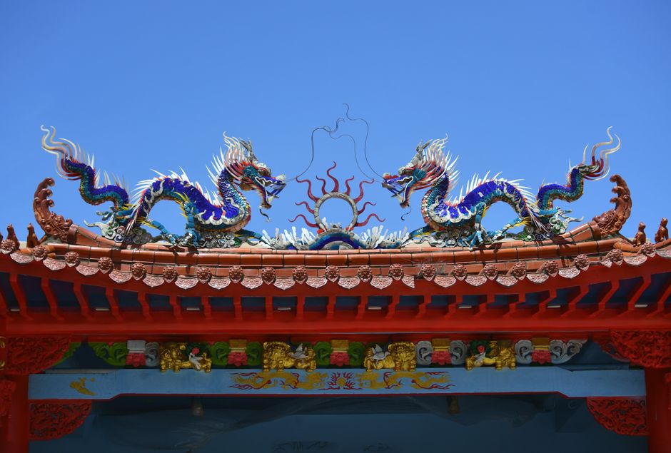 Vibrant dragon sculptures adorn a traditional temple roof under a clear blue sky.