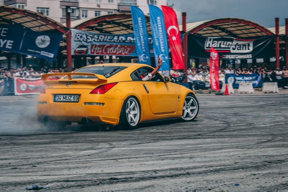 A vibrant yellow Nissan sports car performs a thrilling drift at an outdoor event in Türkiye.