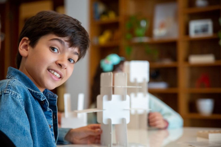 A joyful boy in a denim jacket plays with puzzles indoors, showcasing creativity and fun.