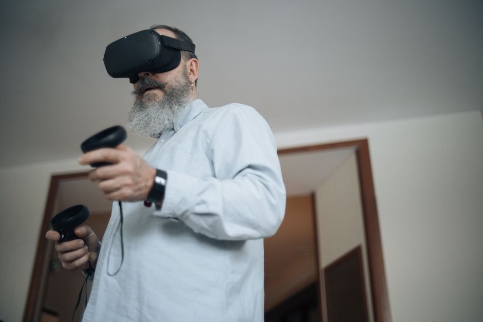 Elderly man wearing VR headset experiencing virtual reality at home.