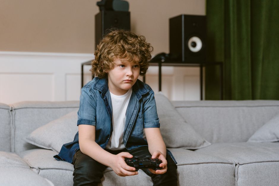 Curly-haired boy intensely playing video games indoors on a comfortable couch.