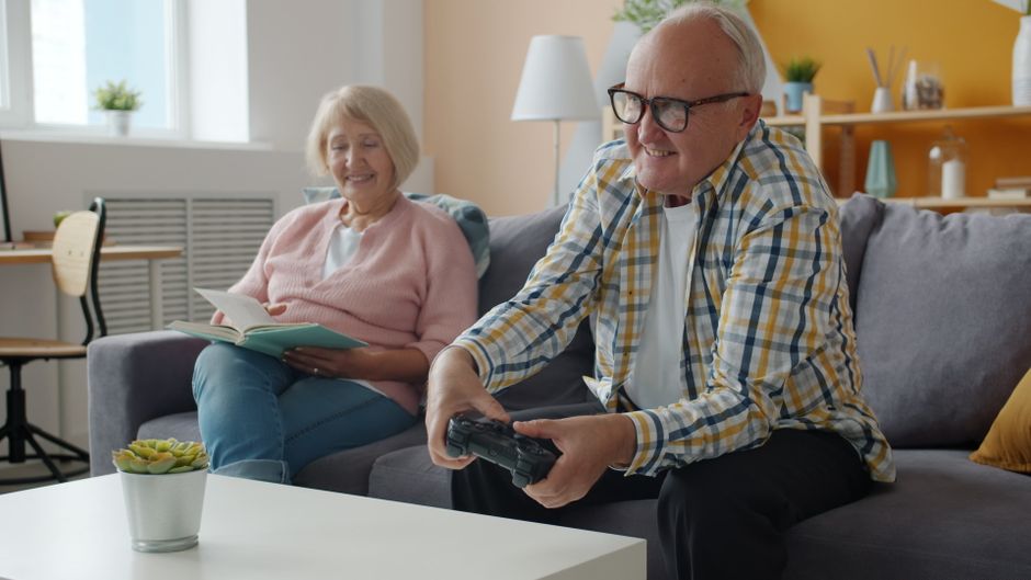 Elderly couple enjoying quality time, gaming and reading in cozy living room.