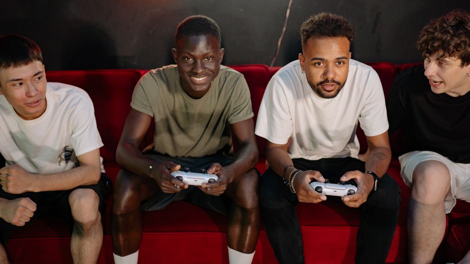 Group of friends having fun playing video games indoors. Diverse group engaging with game controllers on a sofa.