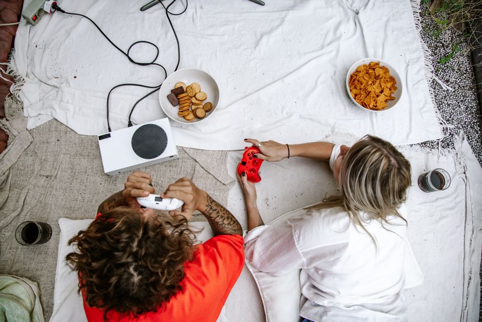 Overhead view of a couple playing video games on a console, surrounded by snacks.