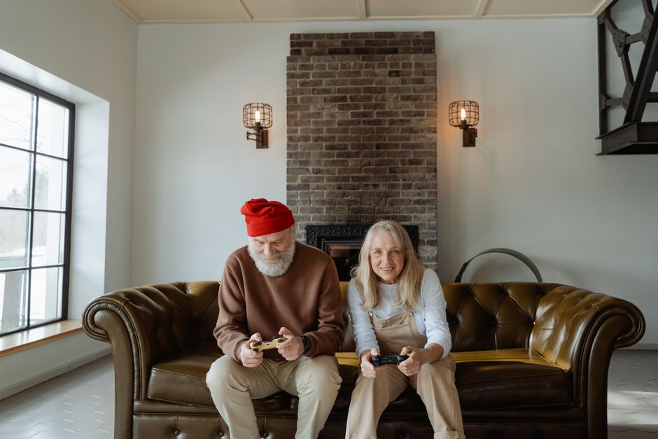 Elderly couple playing video games on the couch in a cozy living room setting.